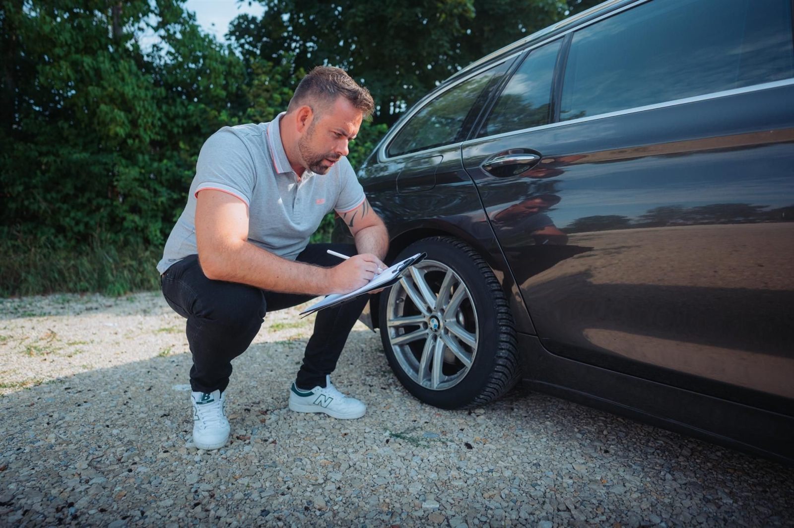 René Richter kniet neben einem dunklen Kombi und notiert Angaben zur Felge auf einem Klemmbrett