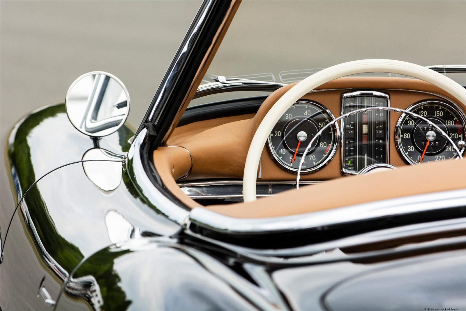 Cockpit eines schwarzen klassischen Cabriolets mit hellbraunem Leder, elfenbeinfarbenem Lenkrad, Chromleisten und runden Instrumenten